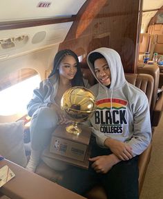 two people sitting on an airplane holding up a basketball trophy and posing for the camera