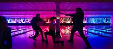 two people standing in a bowling alley with their backs turned to the camera and one person holding a racket