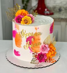 a white cake decorated with flowers and gold lettering