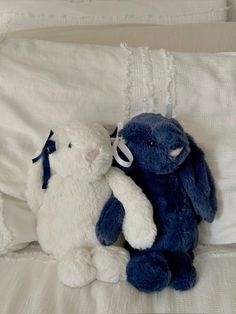 two blue and white stuffed animals sitting next to each other on top of a bed