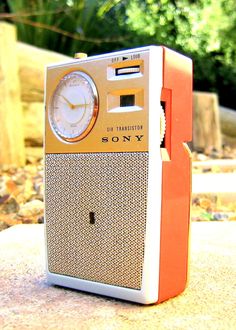 an orange and white radio sitting on top of a cement slab next to trees in the background