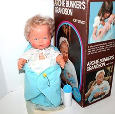 an old doll is sitting next to a box with the baby in it's lap