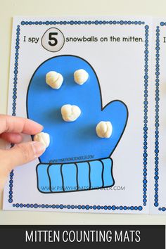 a hand holding a blue mitten counting mats with white snowballs on the mittens