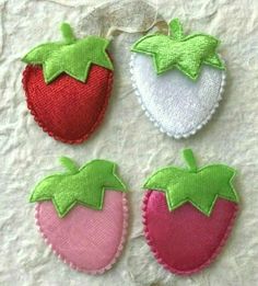 four embroidered strawberrys are sitting on top of a piece of cloth with green and pink trim