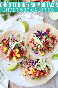 three tacos on a white plate with limes, cilantro and avocado