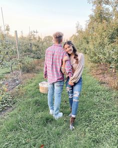 a man and woman walking through an apple orchard