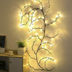 a lighted tree branch on the wall next to a desk with a plant in it