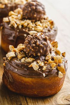 chocolate covered donuts sitting on top of a wooden cutting board with nuts all over them