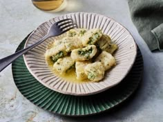 a white plate topped with ravioli and broccoli next to a glass of wine