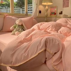 a teddy bear sitting on top of a pink comforter in a room with two windows