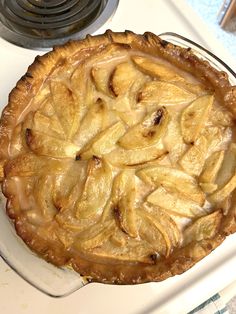 a pie sitting on top of a white stove next to a pan filled with apples