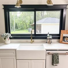 a white kitchen sink sitting under a window next to a wooden frame with pictures on it