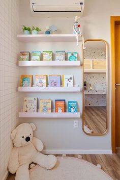 a teddy bear sitting on the floor in front of a bookshelf and mirror