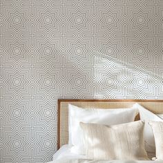 a bed with white sheets and pillows in front of a wallpapered headboard