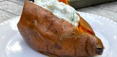 a baked potato on a white plate with sour cream in the center and other toppings