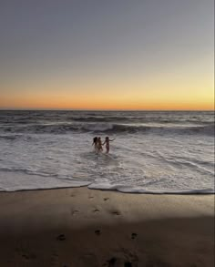 two people are wading in the ocean at sunset