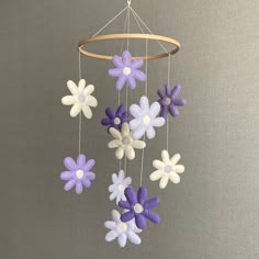 a mobile with purple and white flowers hanging from it's side on a gray background