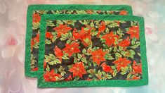 two placemats with red flowers on black and green fabric, sitting on a table