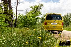 a yellow van is parked on the side of a dirt road near trees and flowers