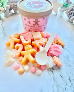 a cup filled with lots of different colored candies next to some spoons and pine cones