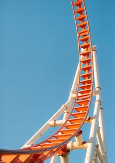 an orange and white roller coaster against a blue sky with no one in sight on it