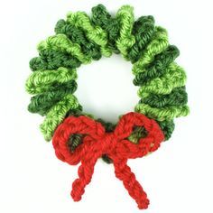 a crochet christmas wreath with red and green yarn tied around it, on a white background