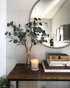 a mirror on the wall above a table with books and a vase filled with flowers