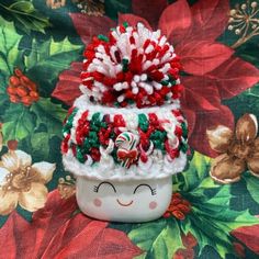 a white cup with red, green and white decorations on it sitting on a floral table cloth