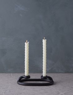 two white candles sitting on top of a black stand