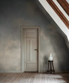 an empty room with a white door in the corner and a wooden stool next to it