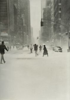 black and white photograph of people walking in the snow on a city street with tall buildings