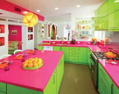 a kitchen with green and pink countertops and cabinets in the center, along with an island that has fruit on it