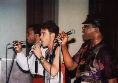 three men singing into microphones while standing next to each other