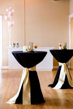 two black tables with white sashes and champagne glasses on them, sitting in a room