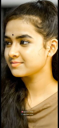 a close up of a person with long hair and wearing a brown shirt looking at the camera