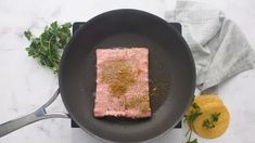 a piece of salmon in a frying pan with parsley and lemons on the side