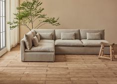 a living room with a sectional couch and wooden flooring next to a large window