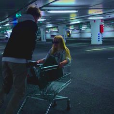 a man pushing a shopping cart with a blonde haired woman in it and another person standing next to him