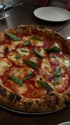 a pizza sitting on top of a wooden table covered in cheese and toppings with green leaves