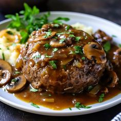 a white plate topped with meat covered in mushroom gravy and mashed potatoes