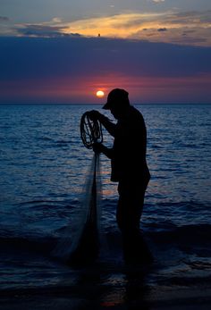 a man standing in the water with a net on his hand and sunset behind him