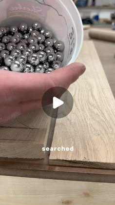 a person holding a bowl full of balls on top of a wooden table next to a piece of wood