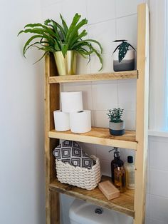 a wooden shelf with toilet paper and plants on it next to a white toilet in a bathroom