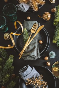 a table topped with black plates covered in christmas decorations and silverware next to pine cones