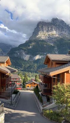 an empty street with mountains in the background and houses on both sides, surrounded by greenery