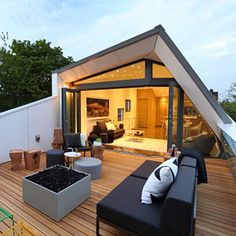 an outdoor living area with couches, tables and chairs on a wooden deck surrounded by trees