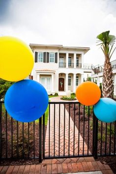 some balloons are hanging on a fence in front of a large white house and palm tree