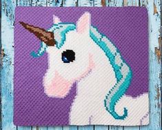 a crocheted unicorn is shown on a purple background with blue wood planks