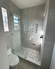 a white toilet sitting next to a shower in a bathroom under a window on top of a tiled floor