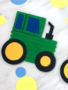 a green tractor made out of construction paper on top of a marble table with circles around it